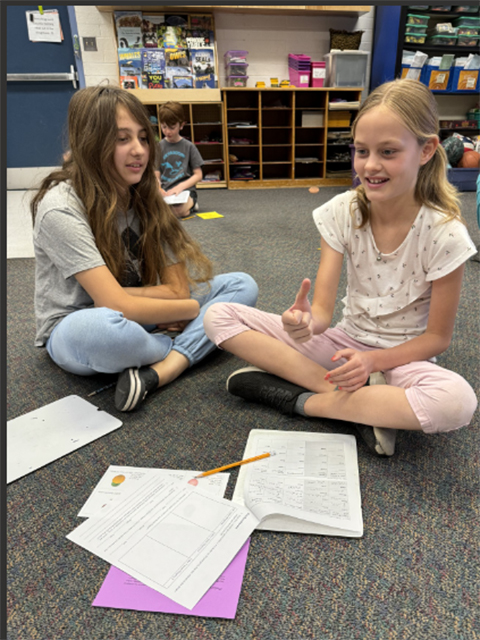 Two students sitting on the classroom floor with worksheets in front of them